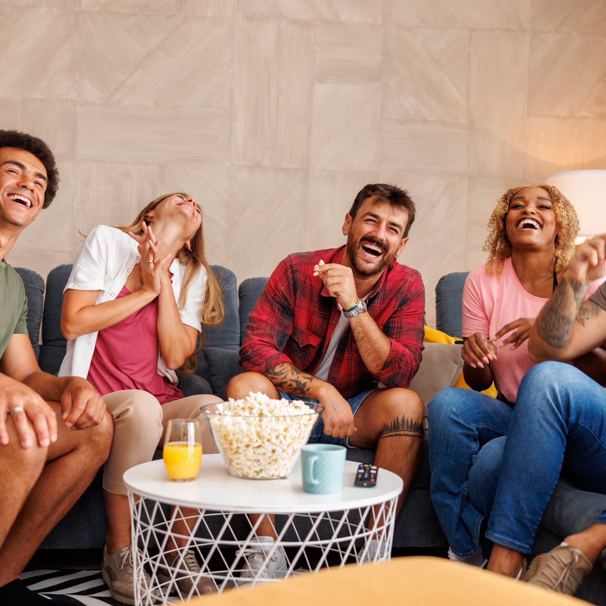 A group of five friends enjoying a fun moment together on a couch, laughing and sharing snacks.