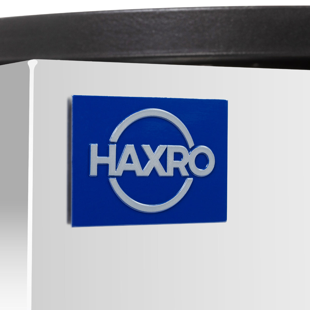 Blue plaque with the word "HAXRO" in bold white letters, encircled by a partial ring, mounted on a sleek, reflective surface.