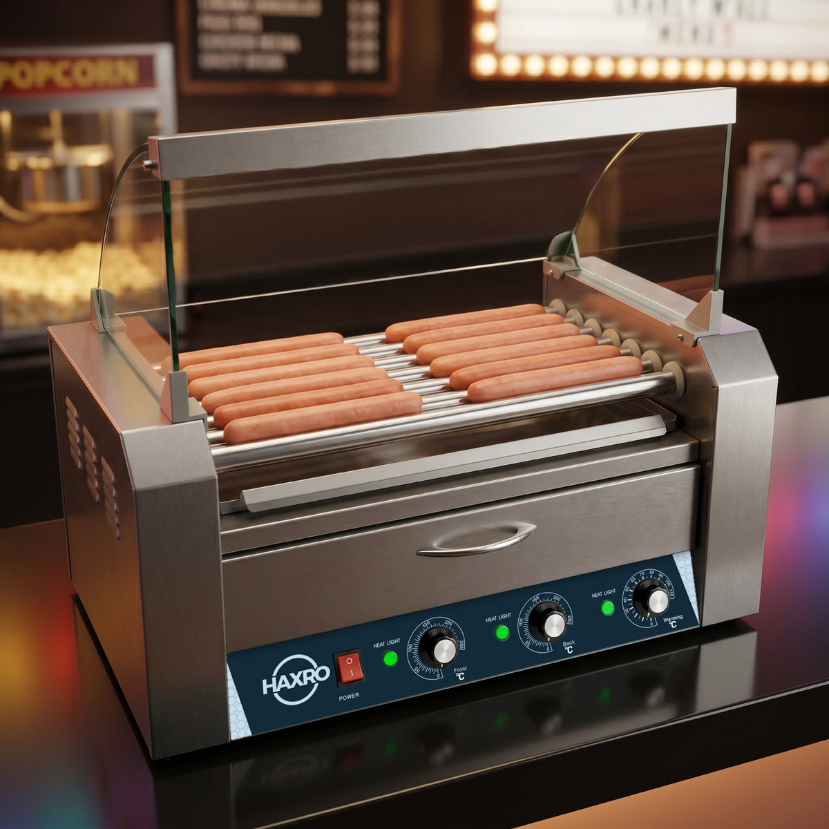 Hot dogs are evenly lined on a stainless steel roller grill with clear glass sides. The machine's control panel is visible, and a popcorn machine is in the blurred background, suggesting a concession stand setting.