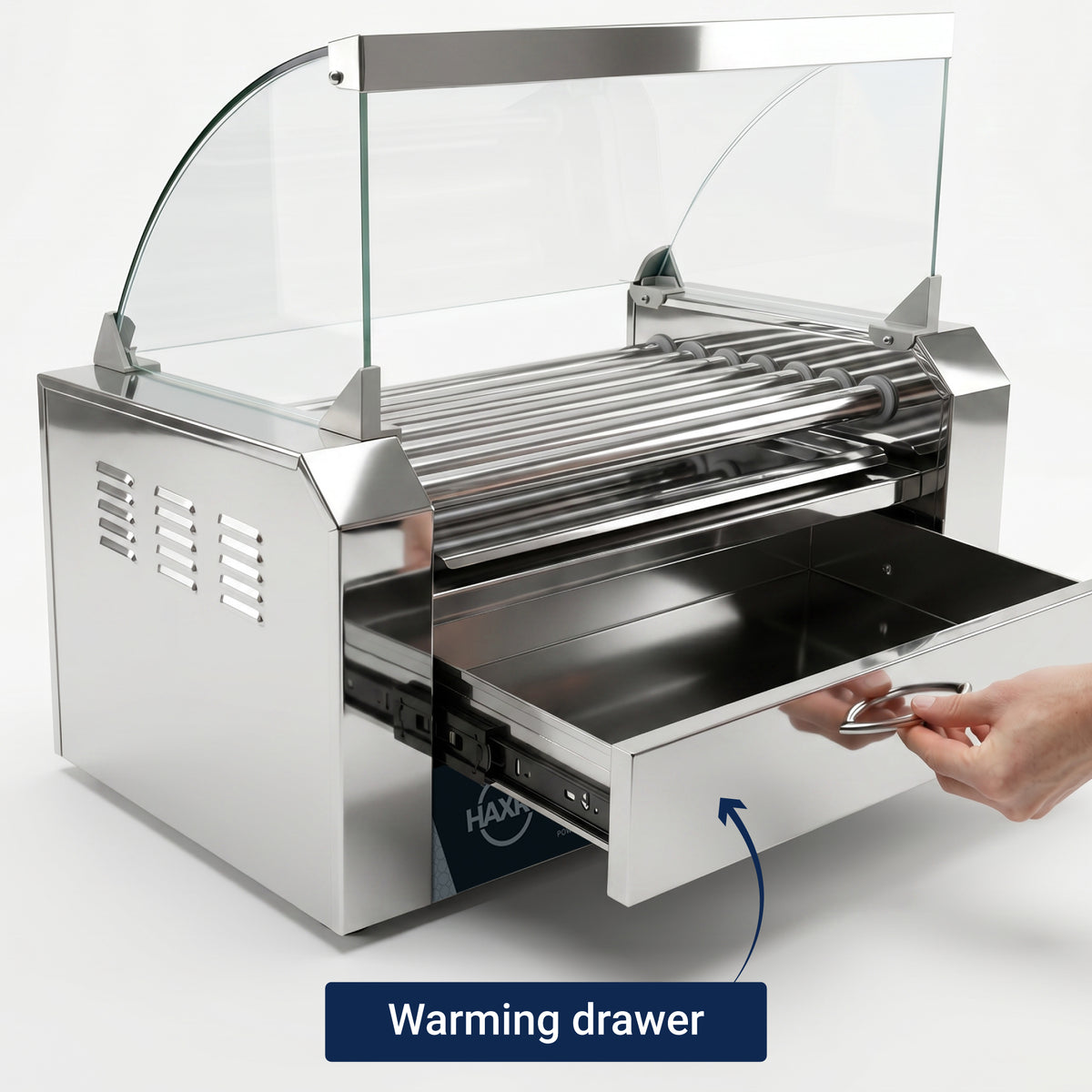 A shiny stainless steel hot dog roller machine with a glass sneeze guard is shown. A hand pulls out the warming drawer below.