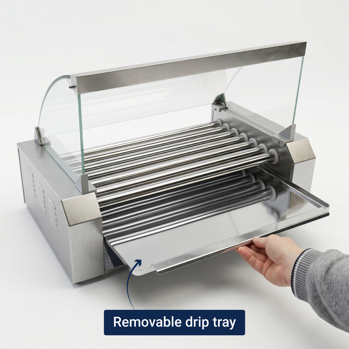 A stainless steel hot dog roller grill with clear glass guard. A hand pulls out the removable drip tray, demonstrating easy cleaning functionality.