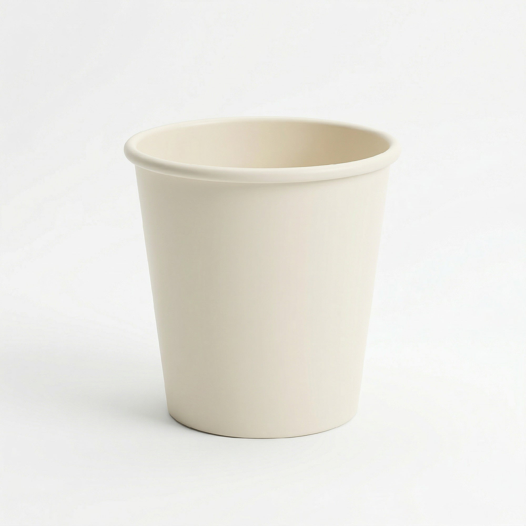 A plain, cream-colored ceramic cup with a smooth surface and a slightly rounded rim, set against a white background, conveying simplicity and minimalism.