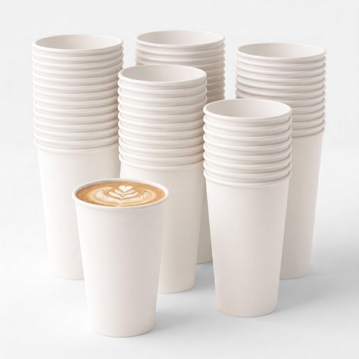 A large stack of plain, white, paper cups fills the background, while in the foreground, a single cup holds a latte with intricate foam art.