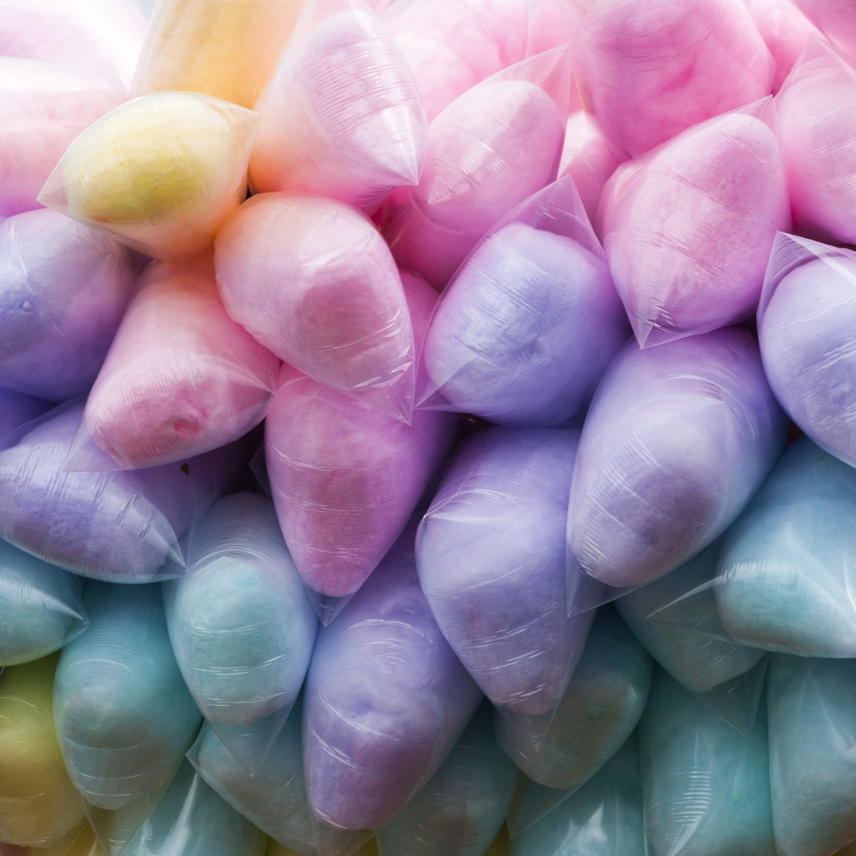 A colorful assortment of cotton candy bags stacked together, featuring shades of pink, blue, purple, and yellow, creating a vibrant and festive display.