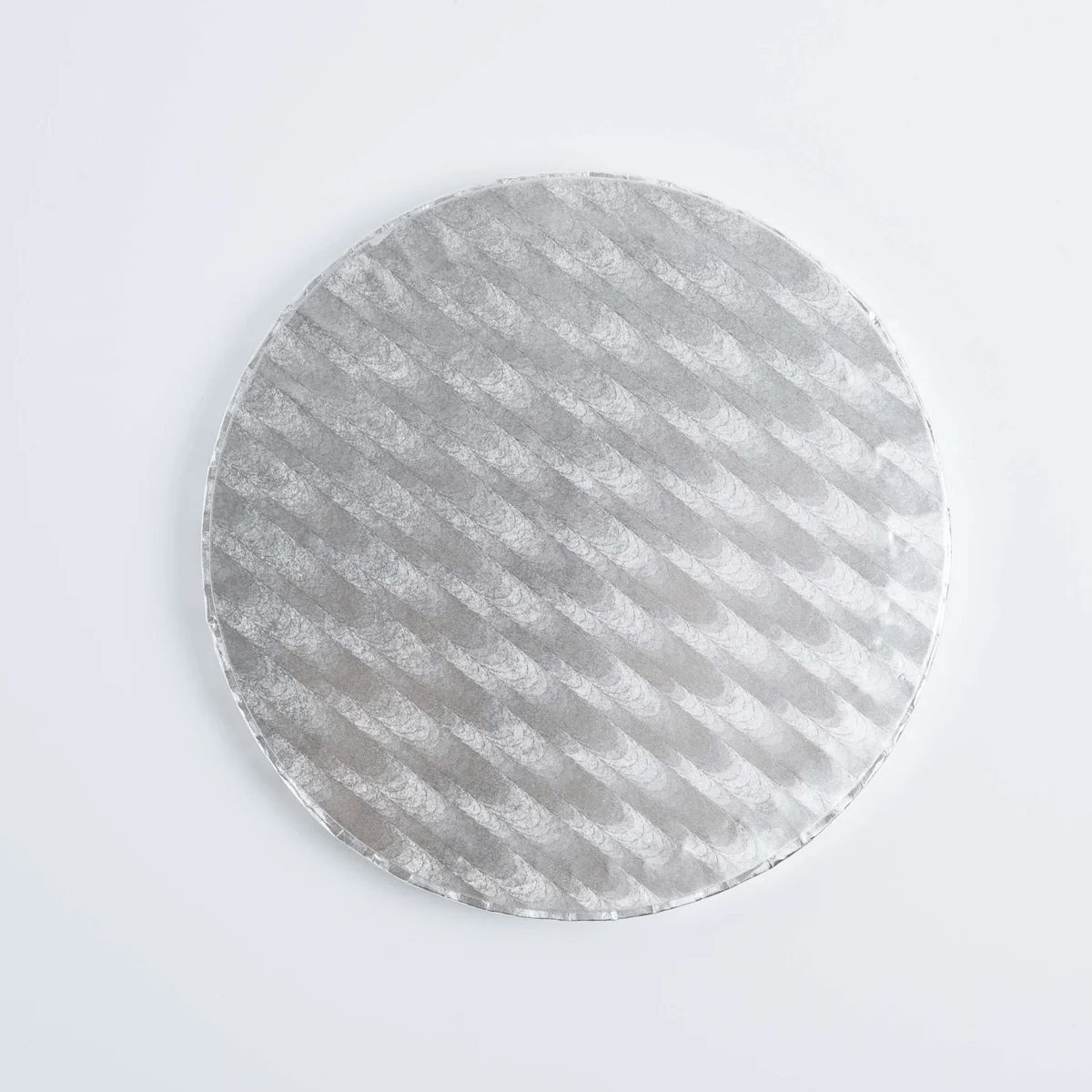 A round silver cake board with a textured diagonal pattern, photographed from directly above on a clean white background.
