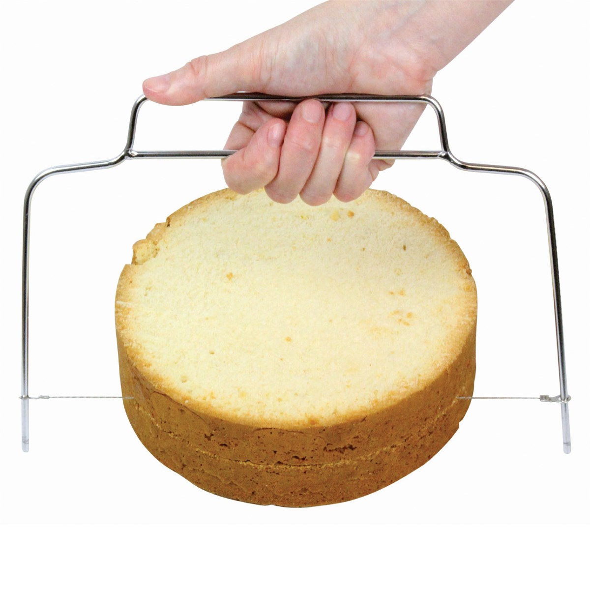 A hand holds a metal cake slicer, evenly slicing a round sponge cake in half. The background is plain white, highlighting the focused action.