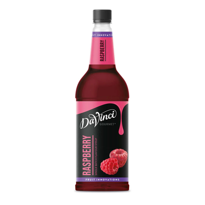 A tall glass bottle of DaVinci Gourmet Raspberry Syrup with a black label and pink accents, showing ripe raspberries on the front and filled with deep red syrup, photographed against a white background.