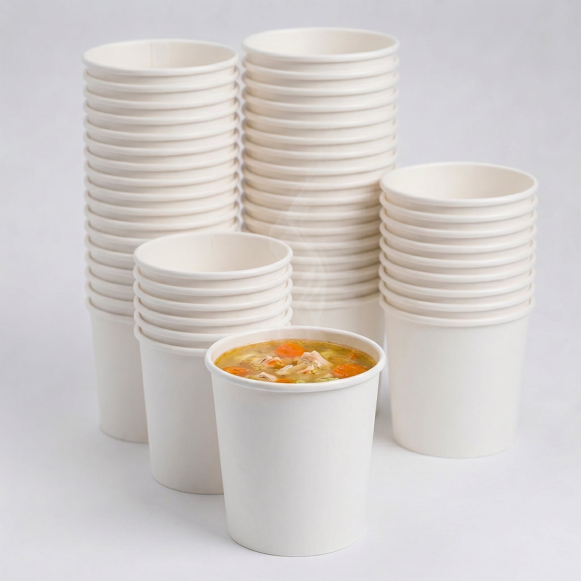 A stack of white paper cups with one filled with steaming chicken noodle soup, featuring carrots and noodles, creating a warm, comforting atmosphere.