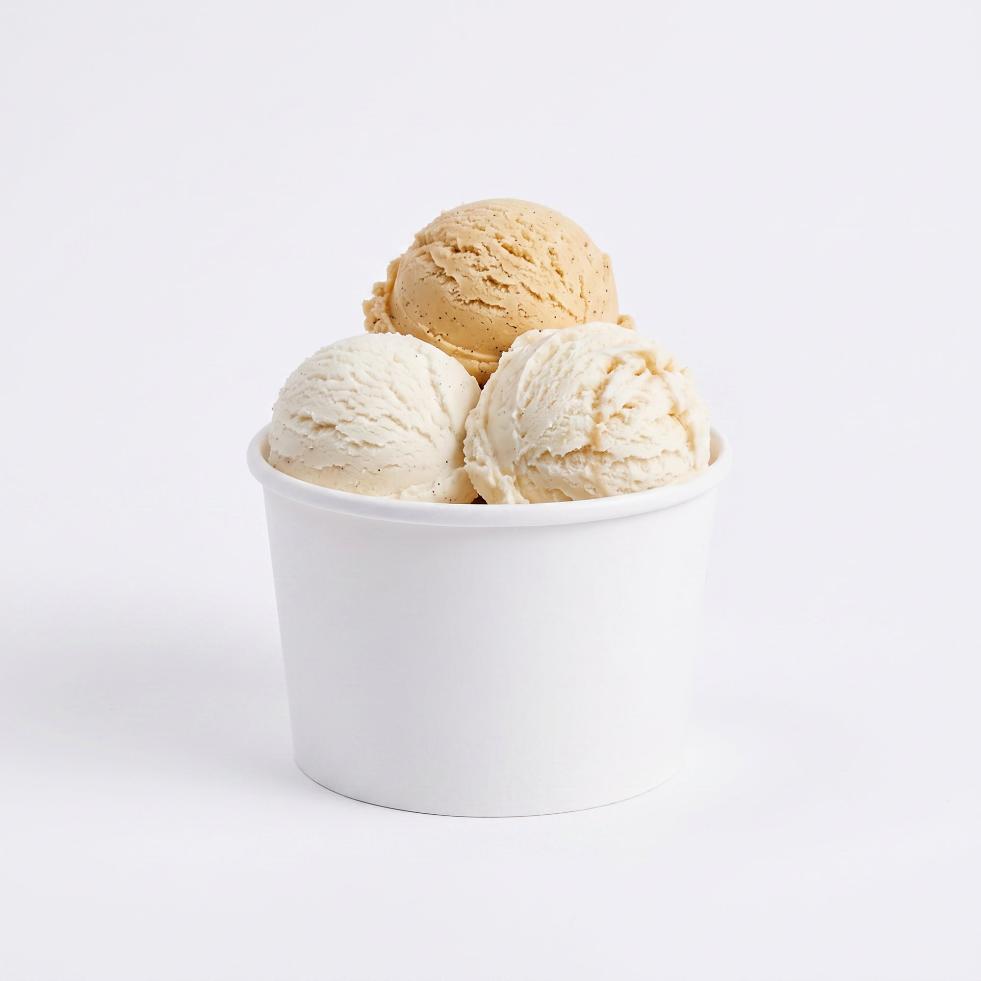 A white cup filled with three scoops of ice cream-vanilla, caramel, and a lighter coffee flavor. Set against a plain white background, evoking a creamy, indulgent tone.