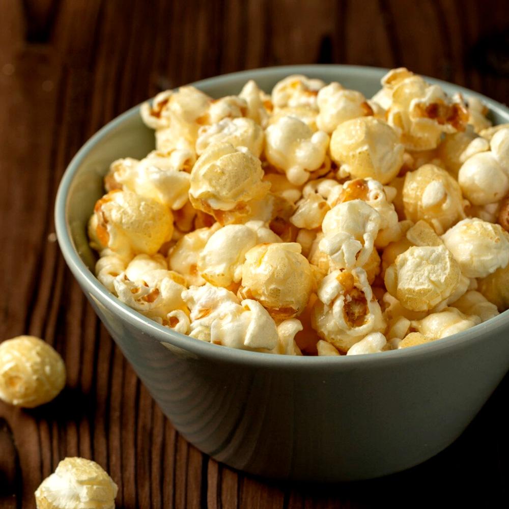 Bowl filled with golden, buttery popcorn on a wooden surface, with a few popcorn pieces scattered nearby.
