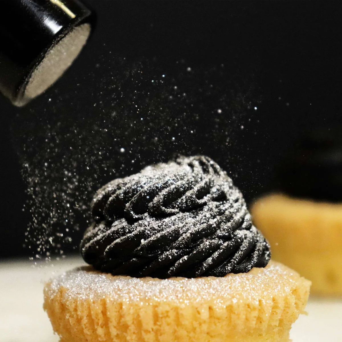 Black dessert being dusted with powdered sugar on a cupcake