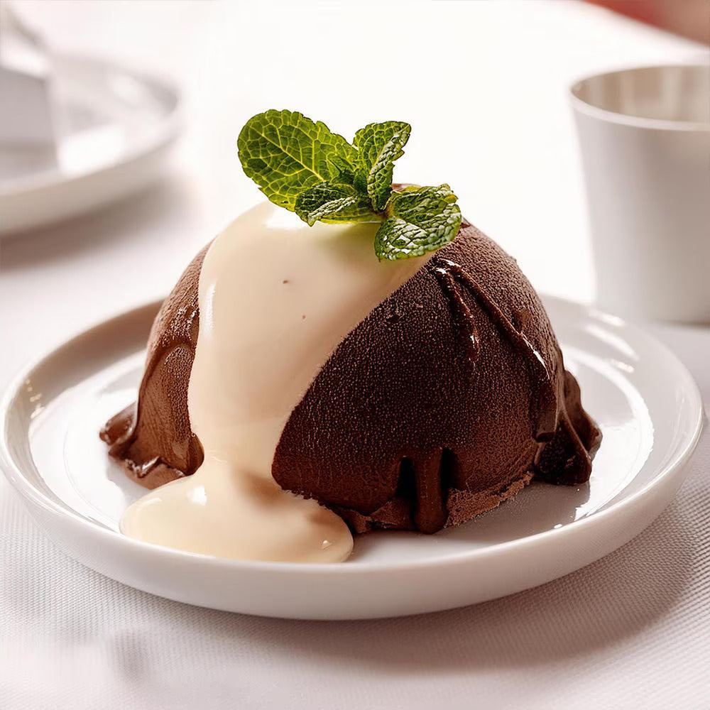 Rich chocolate dome dessert topped with creamy sauce and fresh mint, served elegantly on a white plate, conveying indulgence and elegance.
