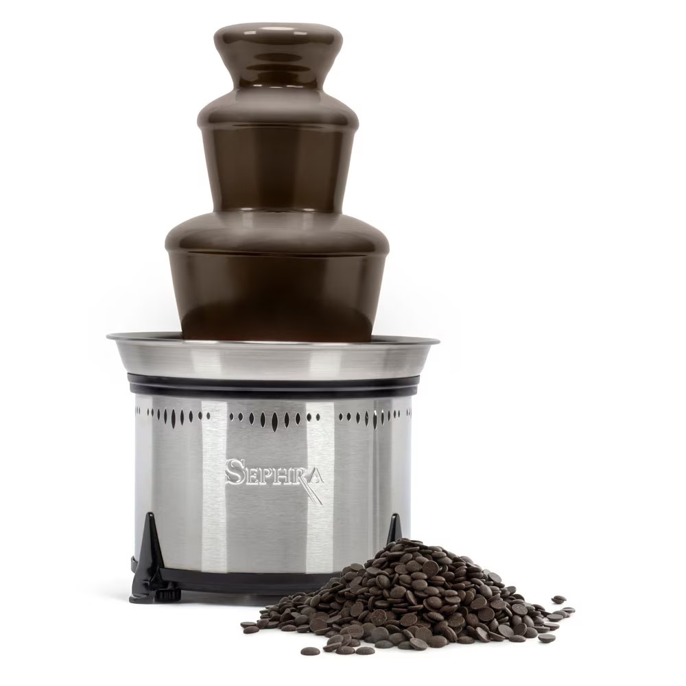 A Sephra stainless steel chocolate fountain filled with flowing dark chocolate, with a pile of chocolate callets placed in front of it.