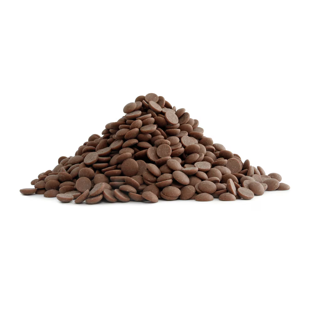A pile of smooth milk chocolate callets or chips arranged on a white surface.