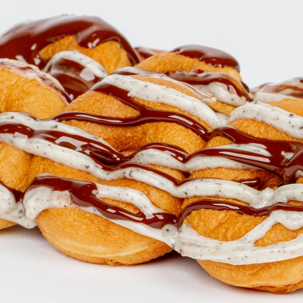 Close-up of golden brown donut balls drizzled with chocolate and cookies-and-cream white sauce.