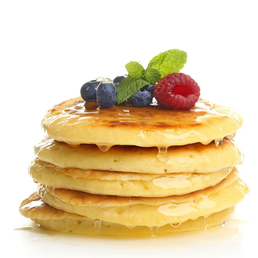 A stack of fluffy pancakes drizzled with syrup, topped with fresh blueberries, raspberries, and a sprig of mint. The pancakes appear moist from the syrup, and the fresh fruits add a pop of color.