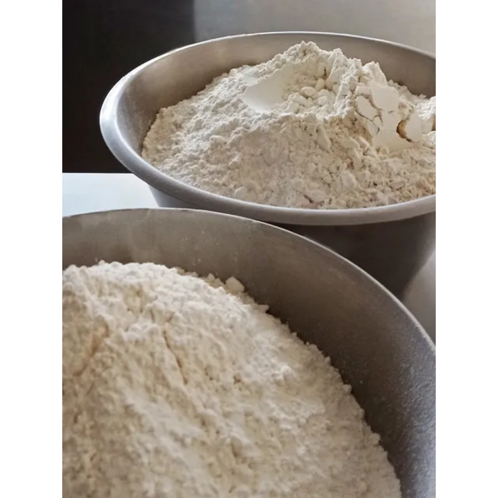 Close-up of two bowls containing different types of flour, with one bowl holding a slightly larger mound of flour than the other.