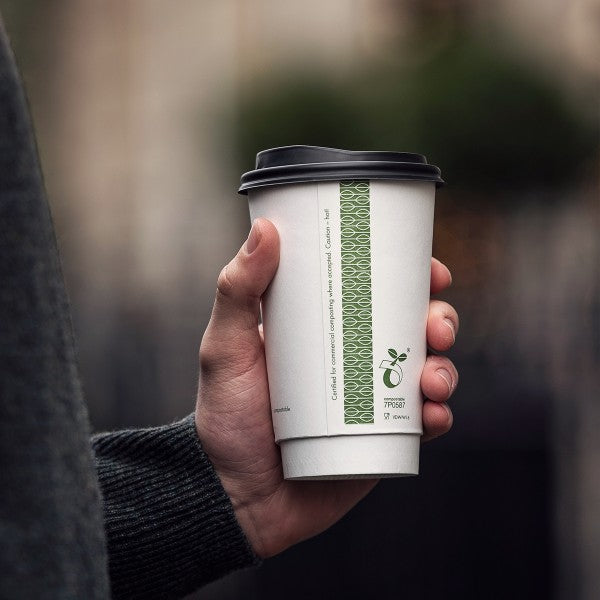 Hand holding a coffee cup with a green patterned sleeve against a blurred background