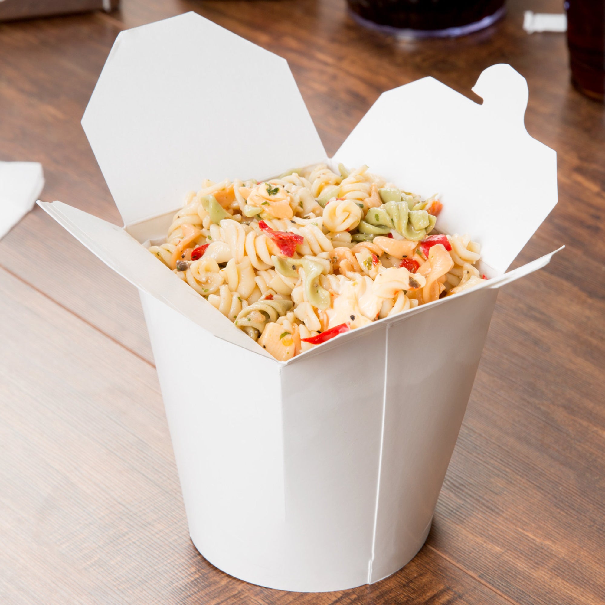 A container of pasta salad with rotini pasta and vegetables.