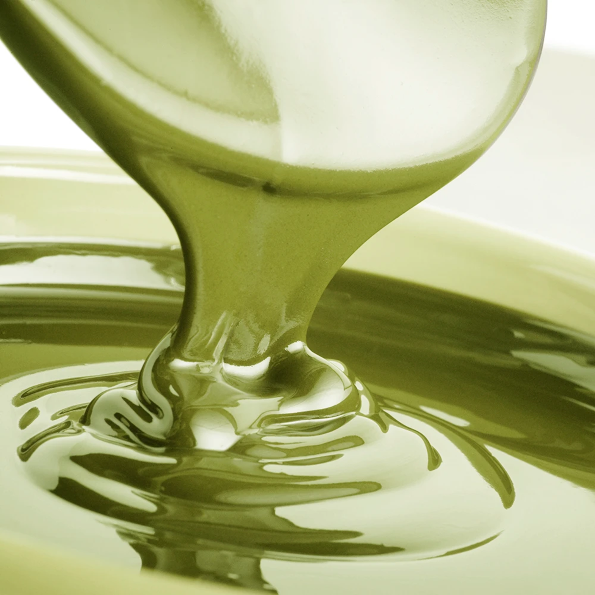 Smooth, green liquid being poured into a bowl, creating ripples and reflections. The glossy texture conveys richness and fluidity.