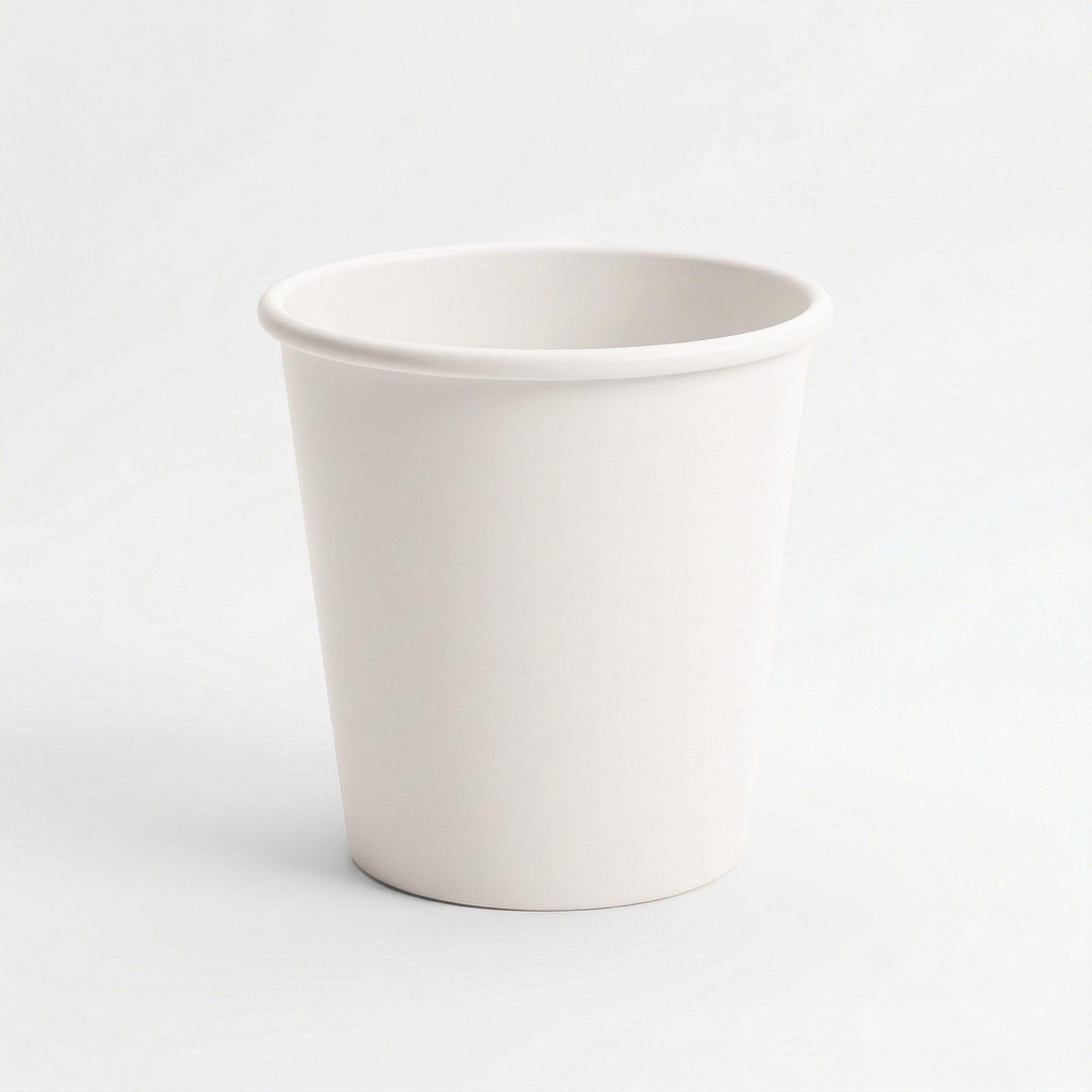 A plain, white-colored ceramic cup with a smooth surface and a slightly rounded rim, set against a white background, conveying simplicity and minimalism.