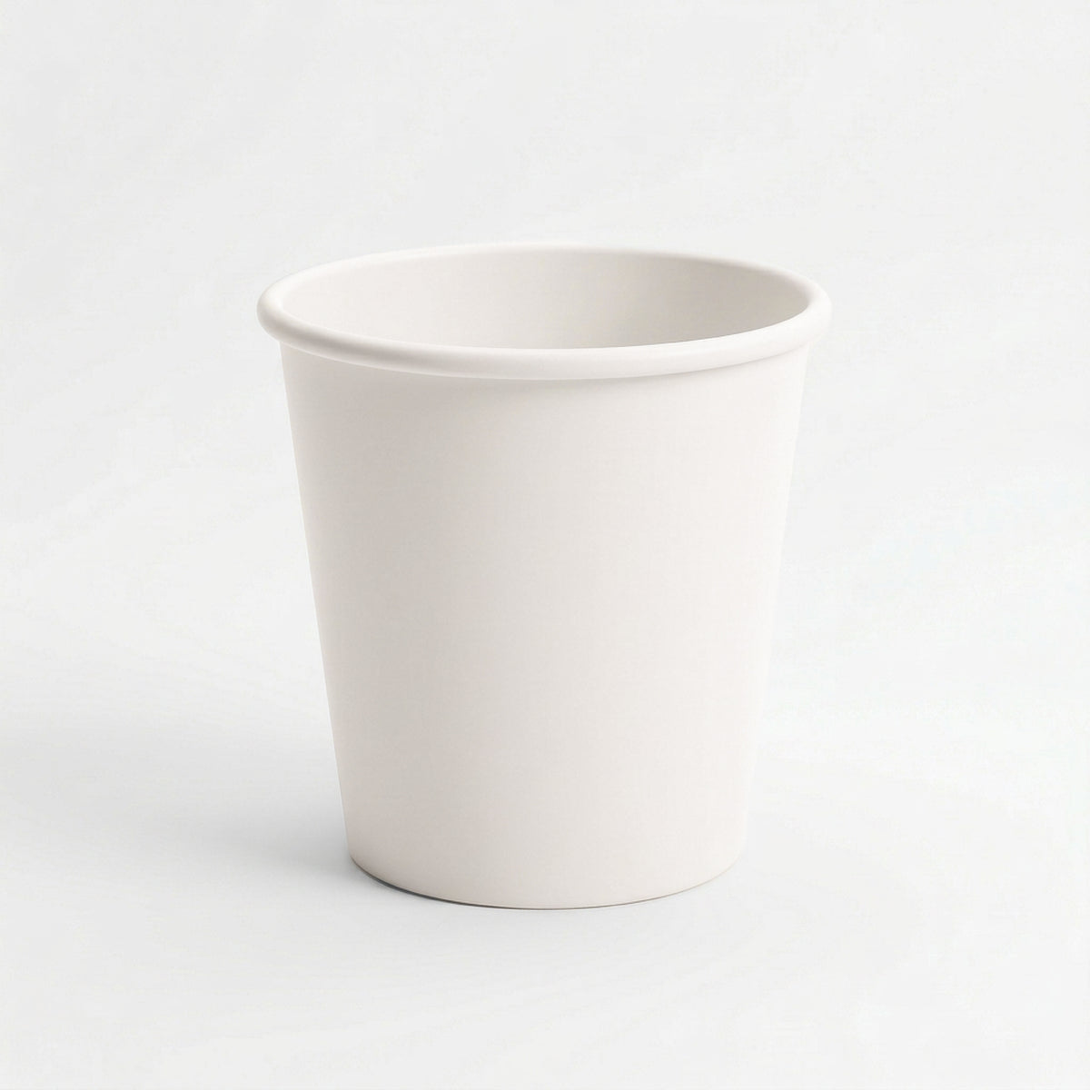 A plain, white-colored ceramic cup with a smooth surface and a slightly rounded rim, set against a white background, conveying simplicity and minimalism.
