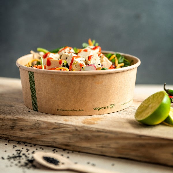 A cardboard bowl filled with a colorful salad, garnished with fresh herbs and a lime.