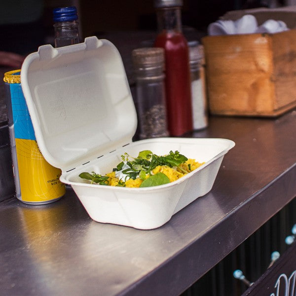 Takeout container with salad on a metal counter with condiments in the background