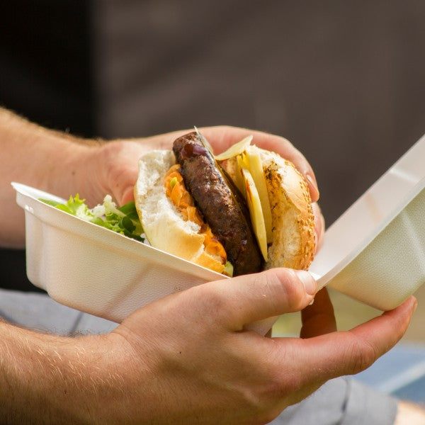 Person holding a burger in a takeout container with a blurred background