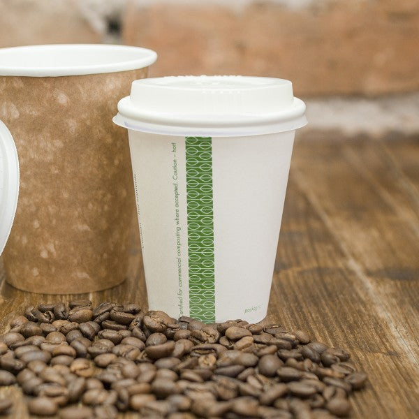 A white disposable coffee cup with a lid, placed on a wooden surface next to a brown cup, surrounded by scattered coffee beans.