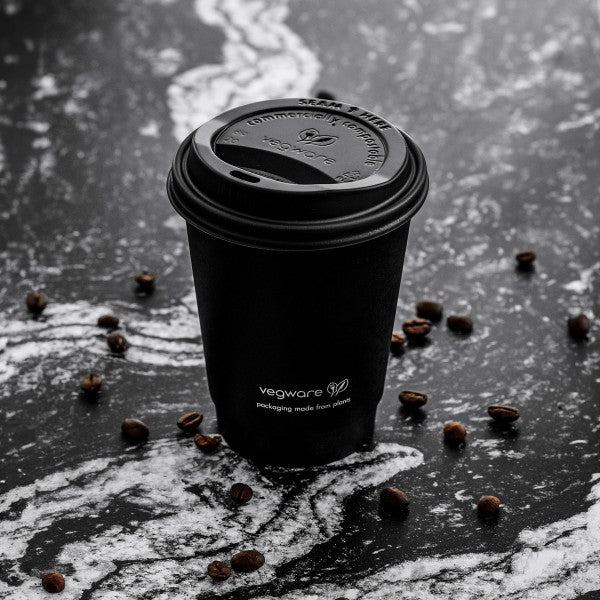 A black coffee cup on a marbled surface surrounded by coffee beans.