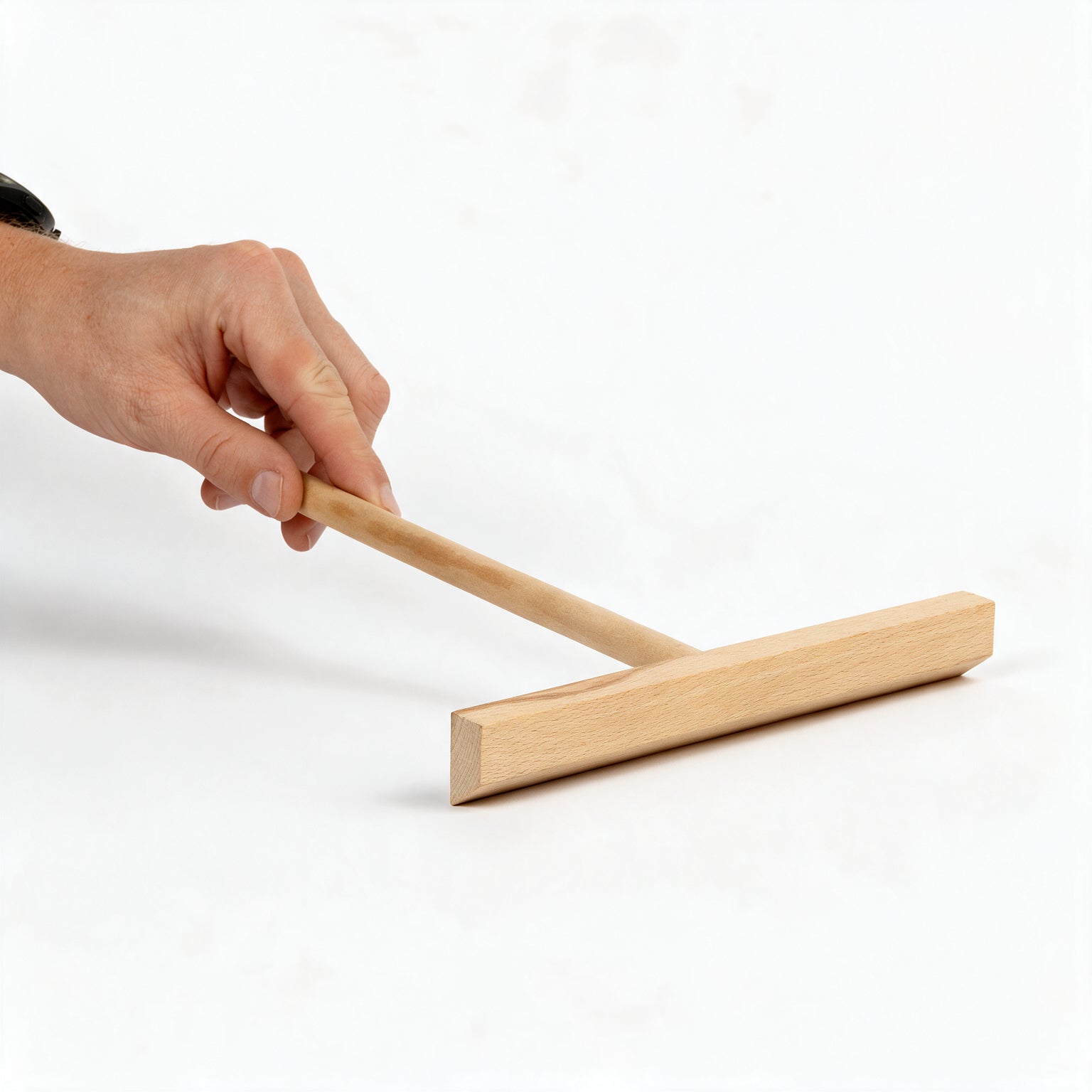 A hand holds the handle of a simple wooden floor squeegee against a clean white surface, suggesting a practical cleaning task in a bright, minimalist setting.